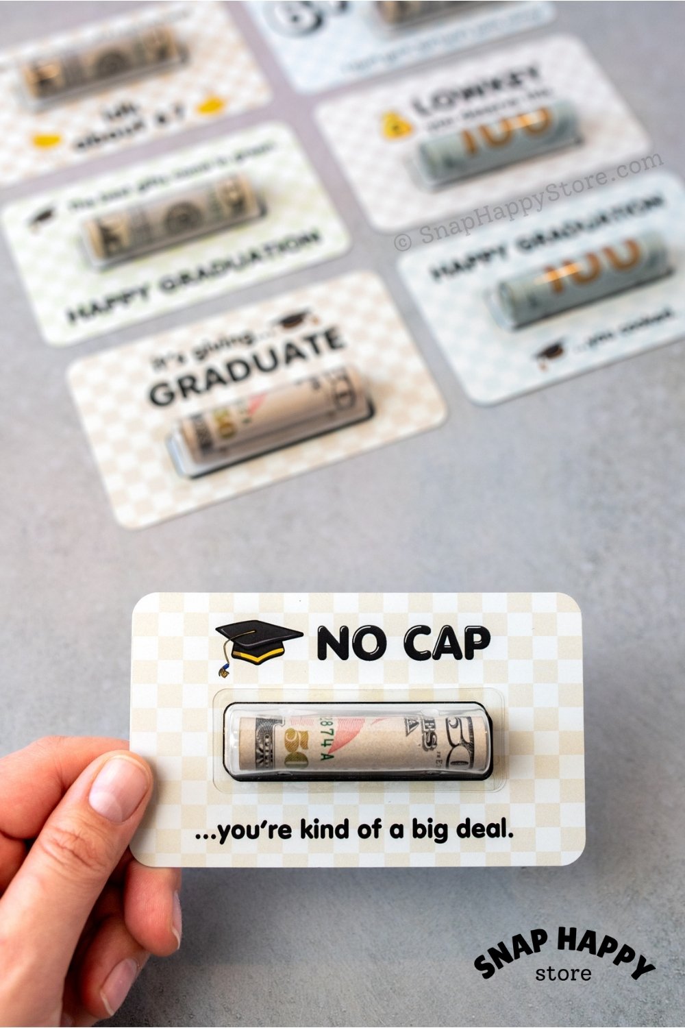 Graduation-themed greeting card with humorous no cap text held by a hand on a gray background